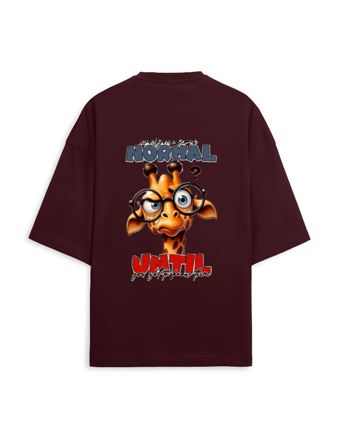 A dark maroon oversized t-shirt with a large graphic print on the back. The graphic features a cartoon giraffe wearing round black glasses, with the text 'is normal UNTIL' in stylized blue and red fonts.