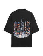 A black oversized short-sleeve t-shirt shown from the back, featuring a large graphic print of the Eiffel Tower and Parisian street scene with the word 'PARIS' in architectural shapes.