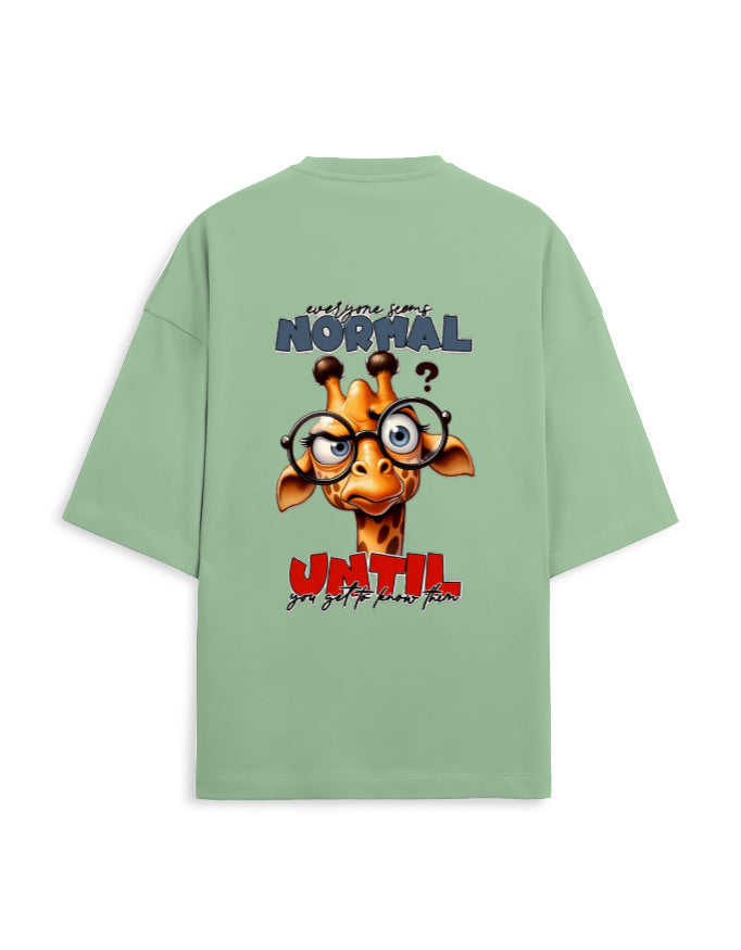 A sage green oversized t-shirt shown from the back, featuring a cartoon giraffe graphic with glasses and the text 'everyone is NORMAL until you get to know you'.