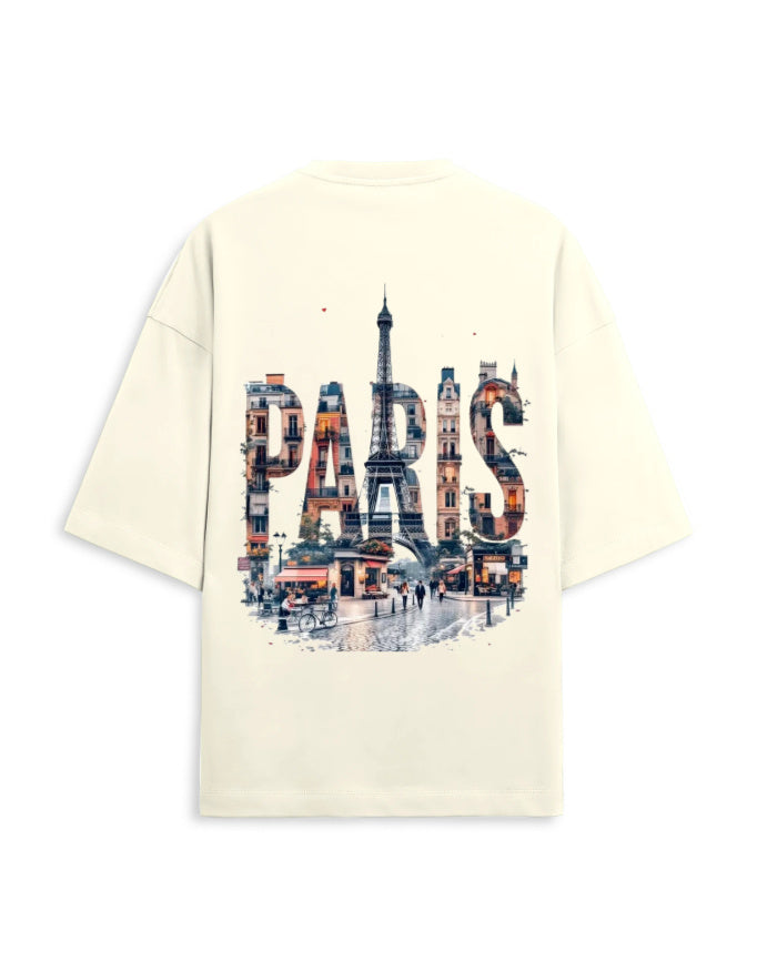 An oversized cream-colored t-shirt shown from the back, featuring a large graphic print of the word 'PARIS' filled with a watercolor-style collage of Parisian scenes, including the Eiffel Tower.