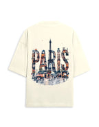 An oversized cream-colored t-shirt shown from the back, featuring a large graphic print of the word 'PARIS' filled with a watercolor-style collage of Parisian scenes, including the Eiffel Tower.