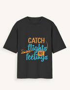 Front view of a dark navy blue unisex oversized streetwear t-shirt featuring a stylized airplane graphic and the text "CATCH FLIGHTS NOT FEELINGS" in orange and teal lettering across the center.