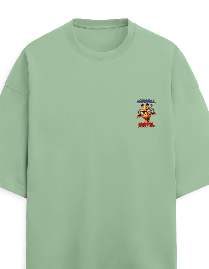 A sage green oversized short-sleeve t-shirt with a small colorful graphic on the left chest featuring cartoon characters and the text 'MORNING' and 'MORNING'.