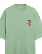 A sage green oversized short-sleeve t-shirt with a small colorful graphic on the left chest featuring cartoon characters and the text 'MORNING' and 'MORNING'.
